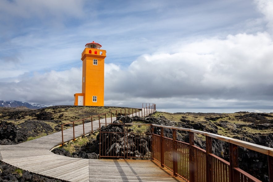 Svortuloft Lighthouse (Svörtuloftsviti), bright orange lighthouse on the westernmost tip of Snaefellsnes peninsula, Iceland with wooden walking platforms for tourists and black volcanic rocks around. 