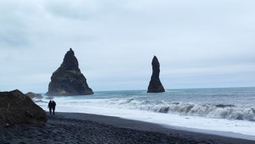 A picture of Reynisdrangar rock formations seen from the shore of the black sand beach.