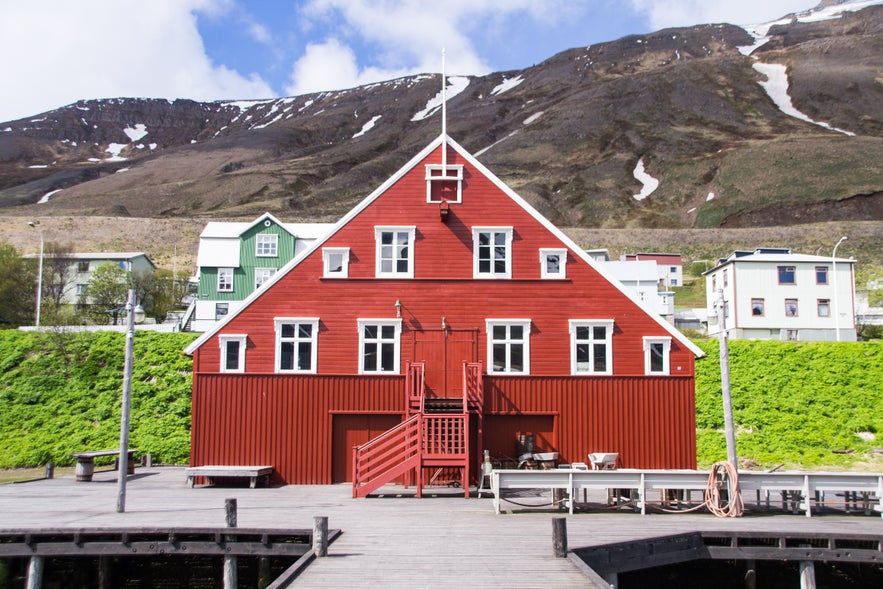 Roaldsbrakki, a historic red wooden building that is part of the Herring Era Museum in Siglufjordur, Iceland. The structure features a steep gable roof, white-trimmed windows, and a central staircase leading to the entrance.