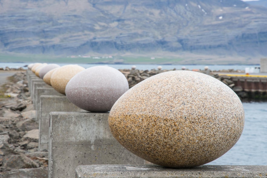 Row of granite bird egg sculptures at Eggin í Gleðivík with fjord and mountains in East Iceland.