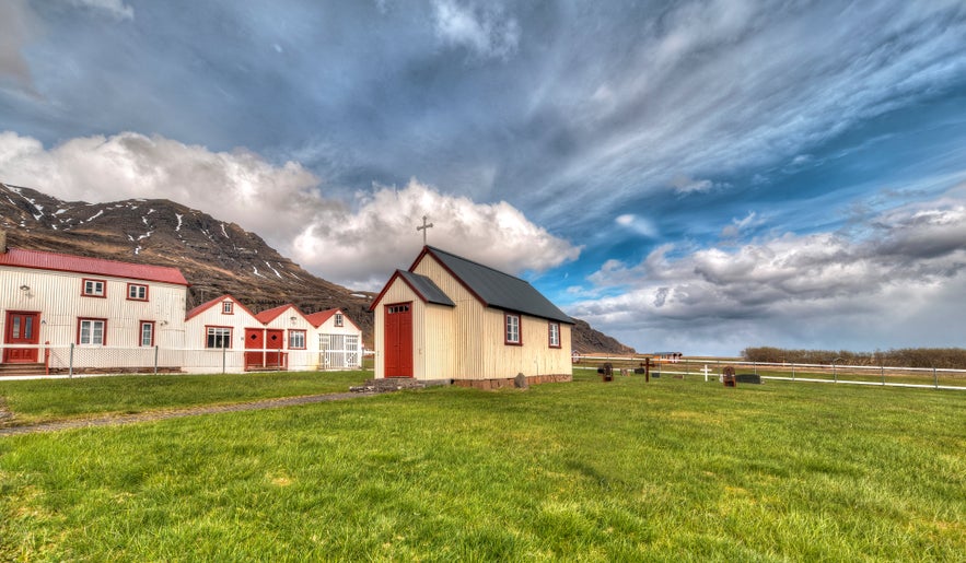 Berunes HI Hostel with red and white buildings set against mountains near Djúpivogur in East Iceland.