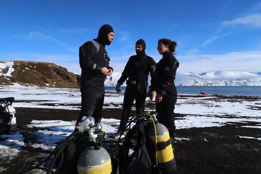 Gruppo di sub con mute stagne che preparano l’attrezzatura subacquea su una riva islandese innevata, con montagne e mare sullo sfondo. Gruppo di sub con mute stagne che preparano l’attrezzatura subacquea su una riva islandese innevata, con montagne e mare sullo sfondo.