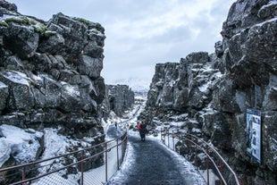 Visitors walk along a path through the snowy, dramatic rock formations of Thingvellir National Park in Iceland during winter.