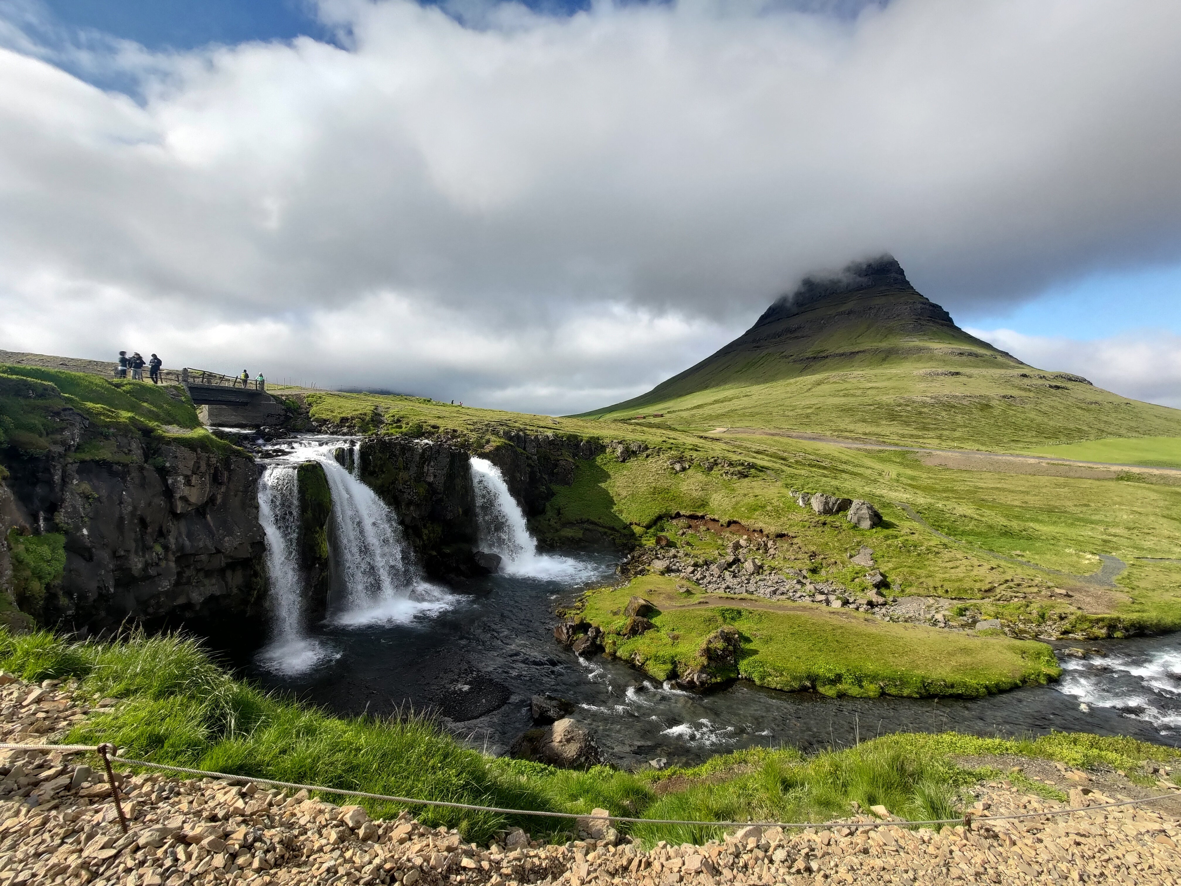 View of Kirkjufell Mountain with mist over the peak and Kirkjufellsfoss Waterfall flowing in front.
