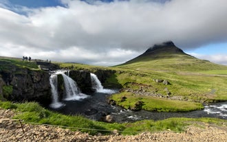 View of Kirkjufell Mountain with mist over the peak and Kirkjufellsfoss Waterfall flowing in front.