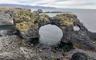 Basalt sea arch and rock formations along the coast near Arnarstapi village.