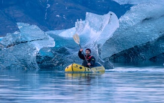 Man paddling a kayak on calm glacier waters with mountain views in Fjallsarlon.
