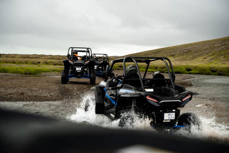 Drei Fahrer auf ATVs überqueren einen Bach.