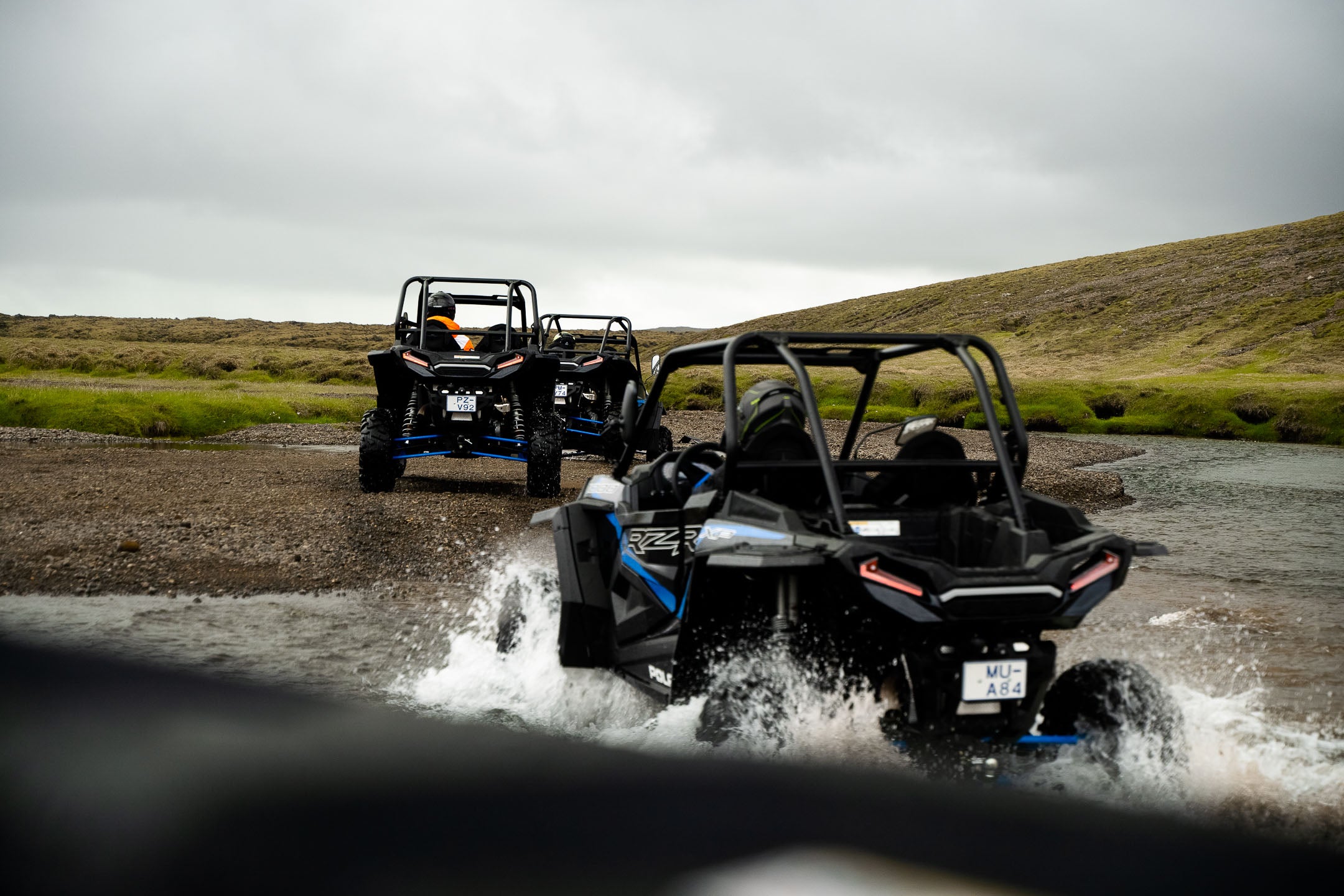 Three riders on ATVs crossing a stream.
