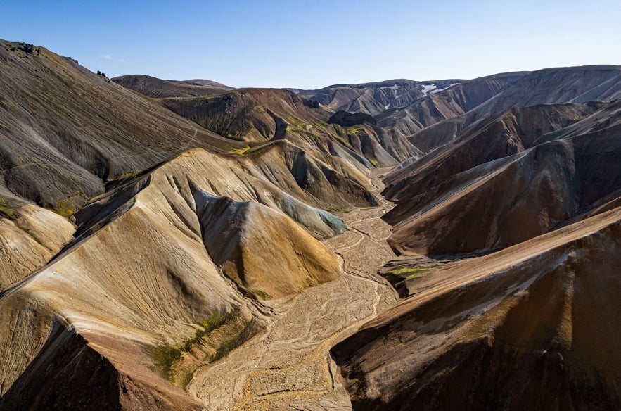 Aerial view of Landmannalaugar in Iceland’s highlands, showing colorful rhyolite mountains and a dry riverbed under clear blue skies.