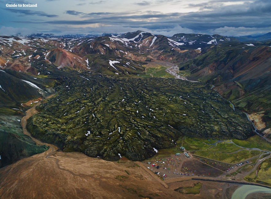 Aerial view of Landmannalaugar campsite and lava field in Iceland’s highlands, surrounded by colorful rhyolite mountains with patches of snow in summer.