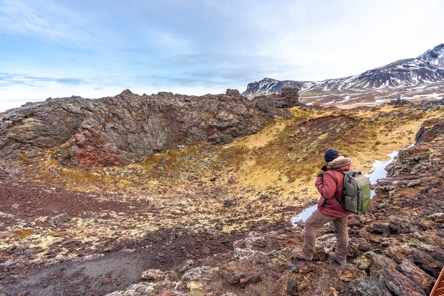 Hiker standing at the edge of Saxholl Crater in Snaefellsjokull National Park, Iceland, admiring volcanic formations and views.