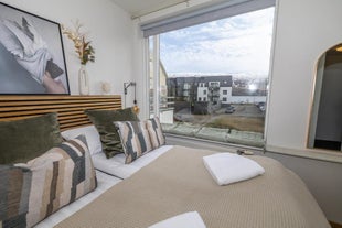 Bedroom with a bedside lamp, and a large window overlooking a building at Charming Deluxe Apartment in Akureyri.