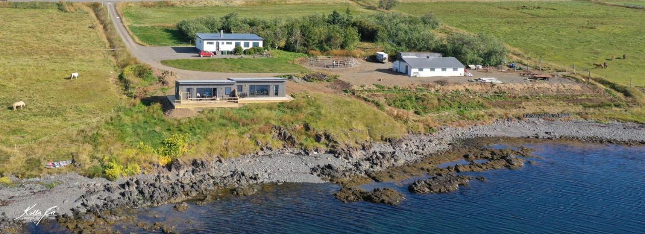 Aerial view of Eyri Seaside Houses in Northwest Iceland and surrounding buildings, grassland, and fjord waters.