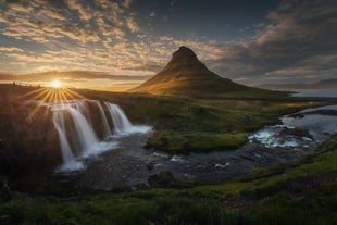 A bright sunset over Kirkjufell Mountain and Kirkjufellfoss Waterfall in the foreground and glowing sky.