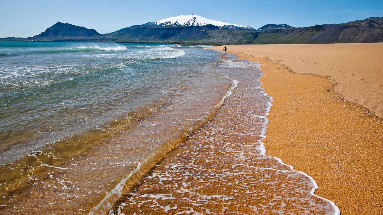 Golden sand beach with waves rolling in and Snaefellsjokull Glacier in the background.
