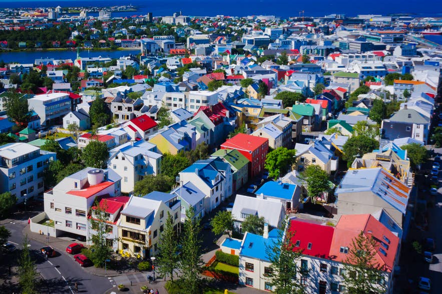 Aerial view of downtown Reykjavik, Iceland, featuring colorful rooftops, residential buildings, and a scenic coastal backdrop on a clear summer day.