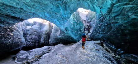 A woman is standing inside an ice cave taking pictures of the blue ice walls.