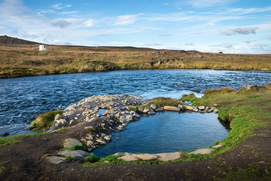 Fosslaug Hot Spring sits in a green landscape during summer.