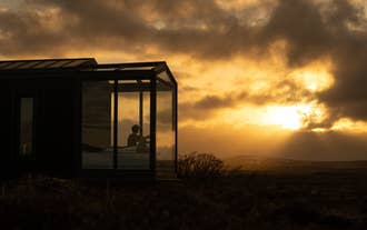 Person watching sunset from bed inside the Tiny Glass Lodge