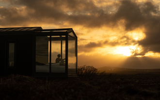Person watching sunset from bed inside the Tiny Glass Lodge