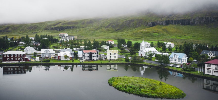 Picturesque town of Seydisfjordur in Iceland’s Eastfjords, featuring colorful houses, a white church, and calm fjord waters under low-hanging mist in summer.