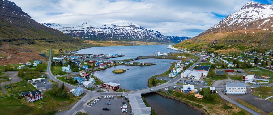Aerial view of Seydisfjordur, Iceland showing buildings, fjords, and surrounding snow-capped mountains.
