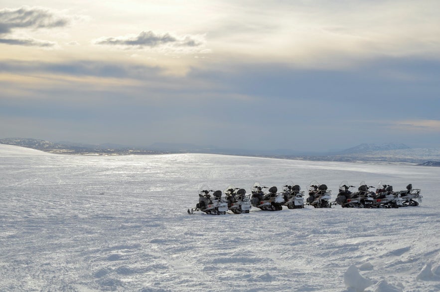 Snowmobiles parked on a vast snowy landscape under a cloudy sky at Langjokull Glacier in Iceland.