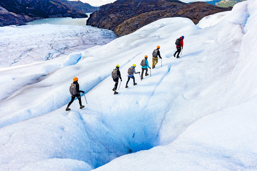 Group of hikers with helmets and ice gear trekking across a glacier in Iceland, surrounded by icy terrain and rugged mountains under clear skies.