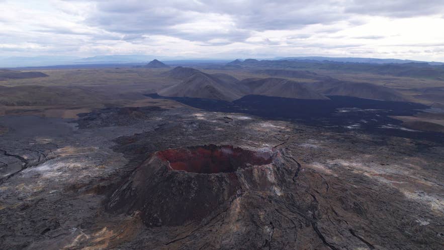 Luchtfoto van de Fagradalsfjall-vulkaan en omliggende lavavelden op het schiereiland Reykjanes in IJsland, met dramatische vulkanische landschappen onder een bewolkte lucht.