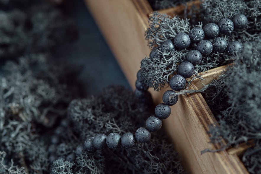 Black lava stone bead necklace resting on dried moss inside a wooden display box, showcasing Icelandic volcanic jewelry.