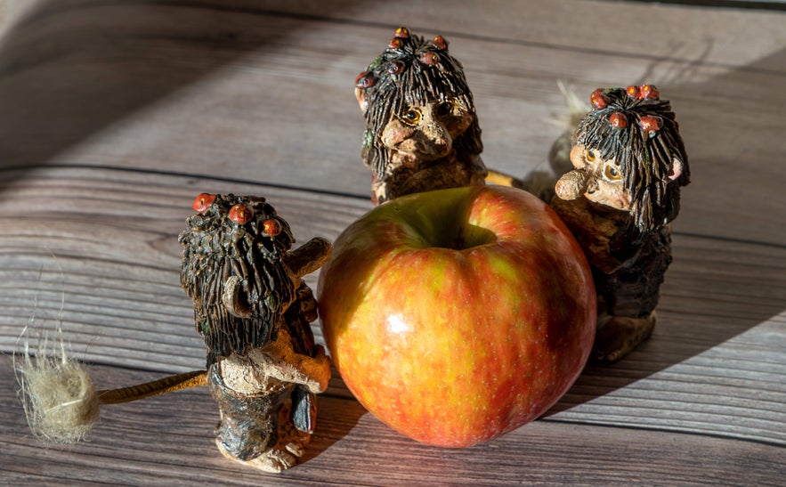 Handcrafted Icelandic troll figurines gathered playfully around a large red apple on a wooden surface.