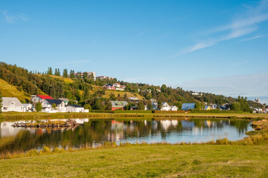 Scenic view of a peaceful lakeside village with colorful houses, lush green hills, and blue sky in Akureyri, Iceland