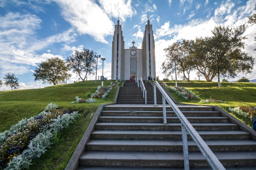 Staircase leading to Akureyri Church (Akureyrarkirkja) with manicured flowerbeds, green lawn, and blue sky in Akureyri, Iceland