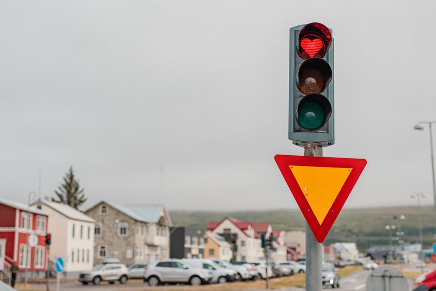 Red traffic light in Akureyri, Iceland, featuring heart-shaped signal above a yield sign on a cloudy day in a charming small town