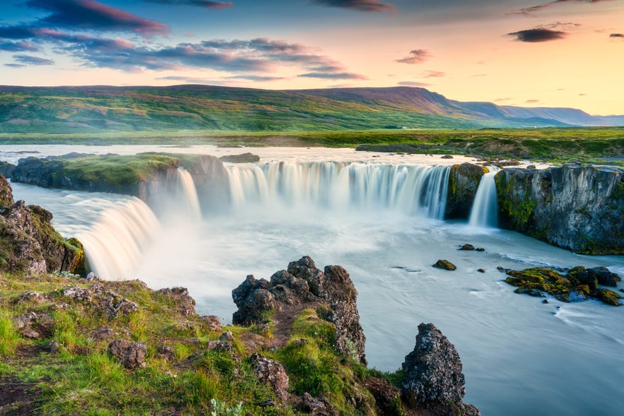 Godafoss waterfall at sunset in North Iceland, with cascading water, volcanic rocks, and scenic mountain backdrop