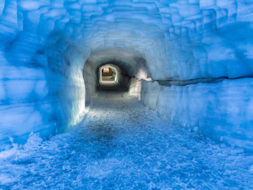 Ice tunnel inside Langjokull Glacier in Iceland, showcasing blue ice walls and a textured frozen floor.