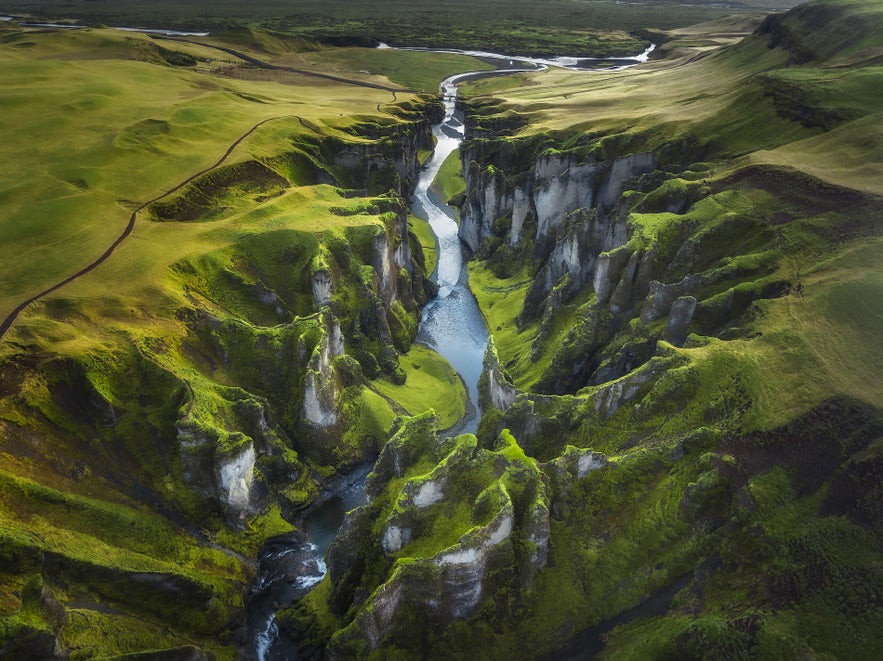 Ilmakuva Fjaðrárgljúfurin kanjonista Etelä-Islannissa, jyrkät sammaleiset kalliot ja mutkitteleva joki vihreässä maisemassa.
