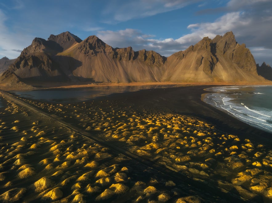 Monta&ntilde;a Vestrahorn y playa de arena negra Stokksnes en Islandia, con dunas doradas y picos dram&aacute;ticos bajo un cielo azul.