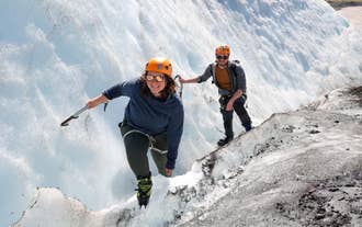 Two travelers hiking on Falljokull glacier in Iceland, wearing cold-weather gear.