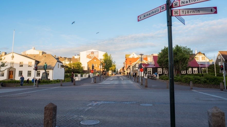 Downtown Reykjavik street scene with colorful buildings, street signs pointing to Arnarhóll and Tjörnin, and pedestrians enjoying a calm summer evening.