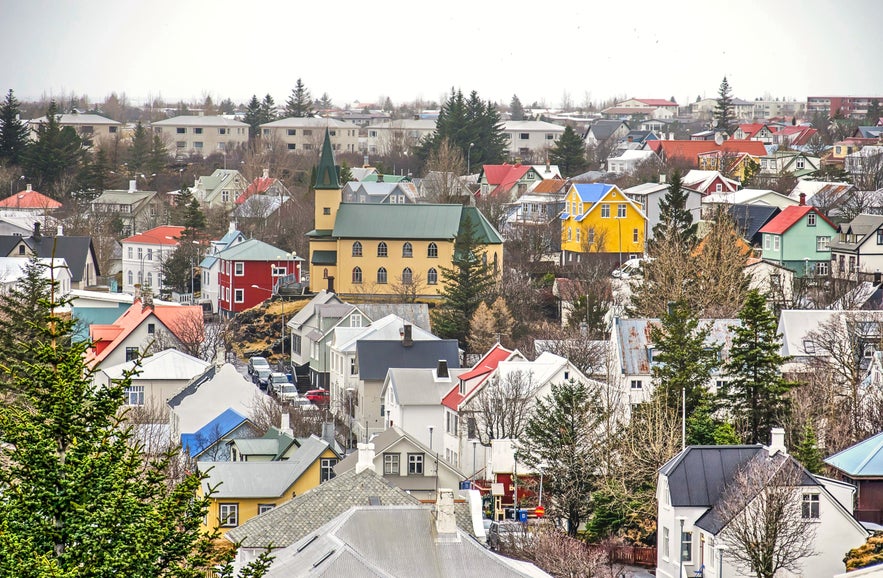 หลังคาบ้านหลากสีสันและบ้านที่มีเสน่ห์ในฮาฟนาร์ฟยอร์ดูร์ ประเทศไอซ์แลนด์ พร้อมด้วยต้นไม้ใบโกร๋นและท้องฟ้าที่มีเมฆปกคลุมอ่อนๆ ในช่วงต้นฤดูใบไม้ผลิ