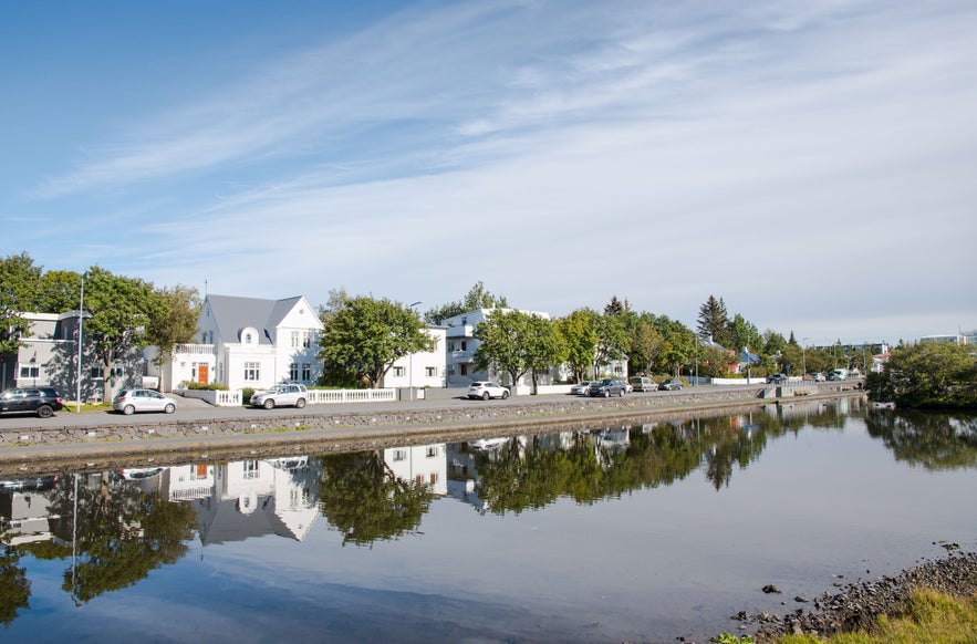 White and pastel-colored houses reflecting in the still waters of the Hafnarfjordur Lake under a bright blue sky in the Capital Area, Iceland.