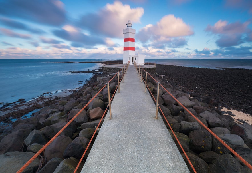Pathway leading to the striped white and red Gardur Lighthouse on the rocky coast near Keflavik.