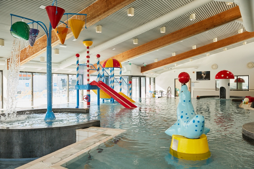 Colorful indoor play pool at the Keflavik swimming center with water slides, tipping buckets, and a seal statue fountain.