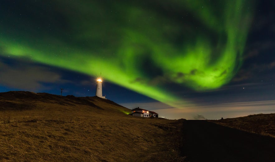 Northern lights glowing above Reykjanesviti Lighthouse near Keflavik on a dark hilltop night.