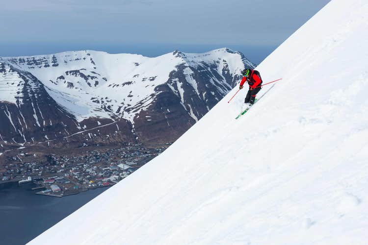 A tour participant skiing on the slopes of Trollaskagi, with a town seen below.