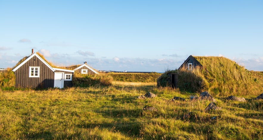 Traditional turf houses with grass-covered roofs in a sunlit field near Keflavik.