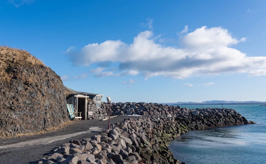 Rocky path leading to the entrance of the Giantess in the Cave attraction in Keflavik, with a small hut built into the cliffside by the ocean.