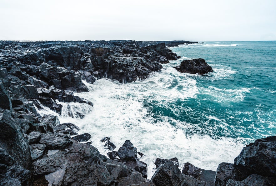 Waves crashing against black volcanic rocks along the rugged coast of the Reykjanes Peninsula.